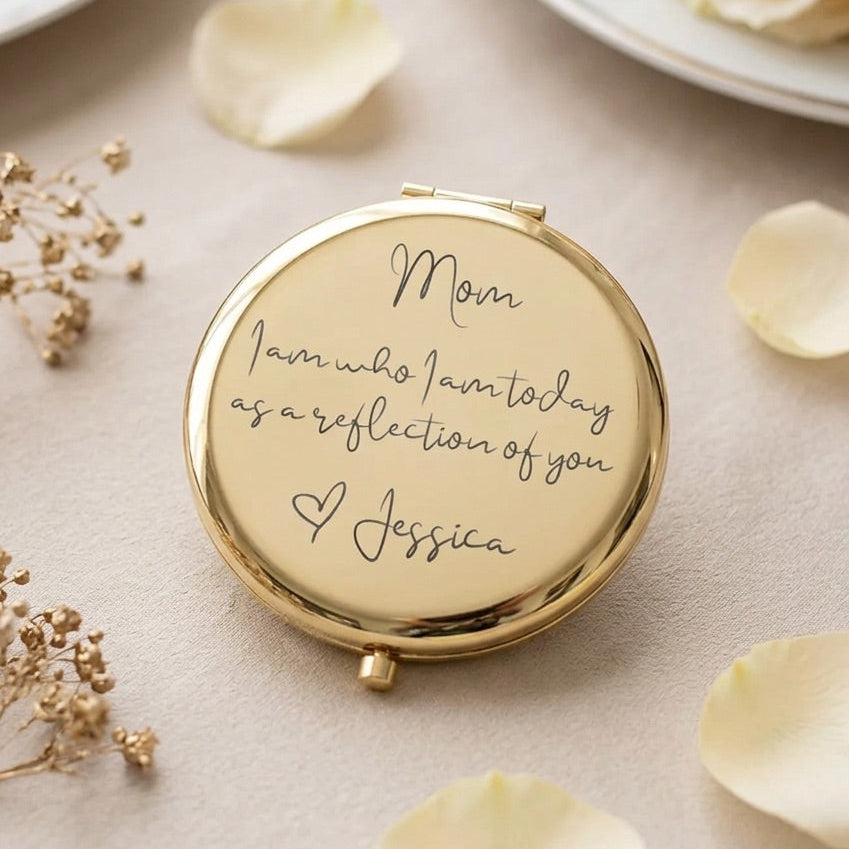 A round gold compact mirror engraved with the message 'Mom I am who I am today as a reflection of you' and the name 'Jessica', styled on a beige surface with dried flowers and rose petals.