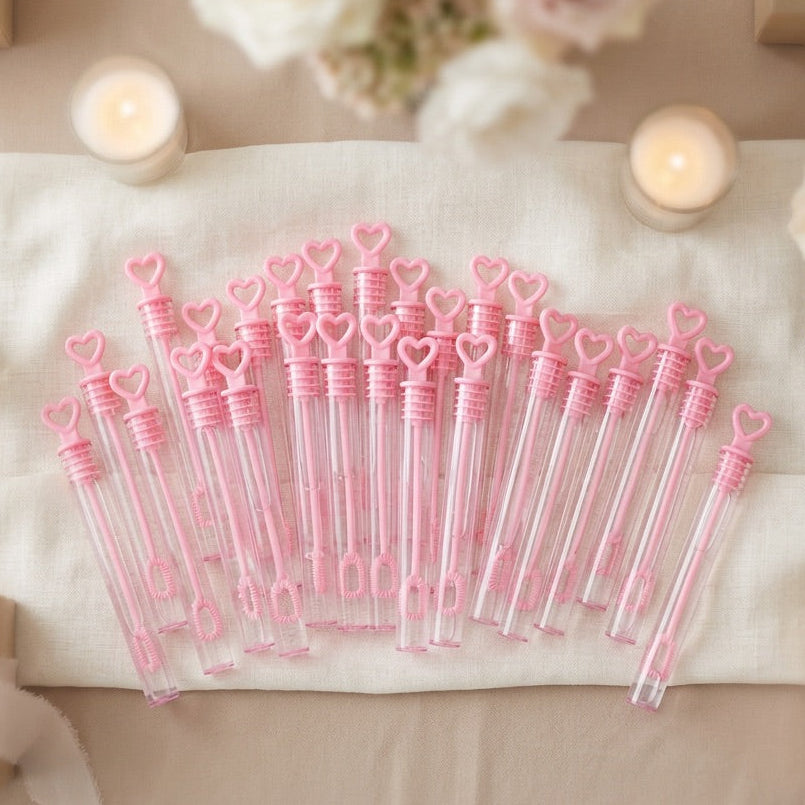 Set of pink and clear bubble wands with heart designs on a decorative table with candles and flowers.