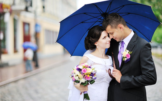 Bride and groom embracing under umbrellas on a rainy wedding day