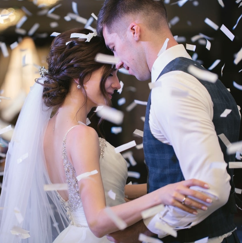A decorated wedding reception table, complete with food and 2 mini bottles of wine, one with a little bride's dress cover, the other a tuxedo.