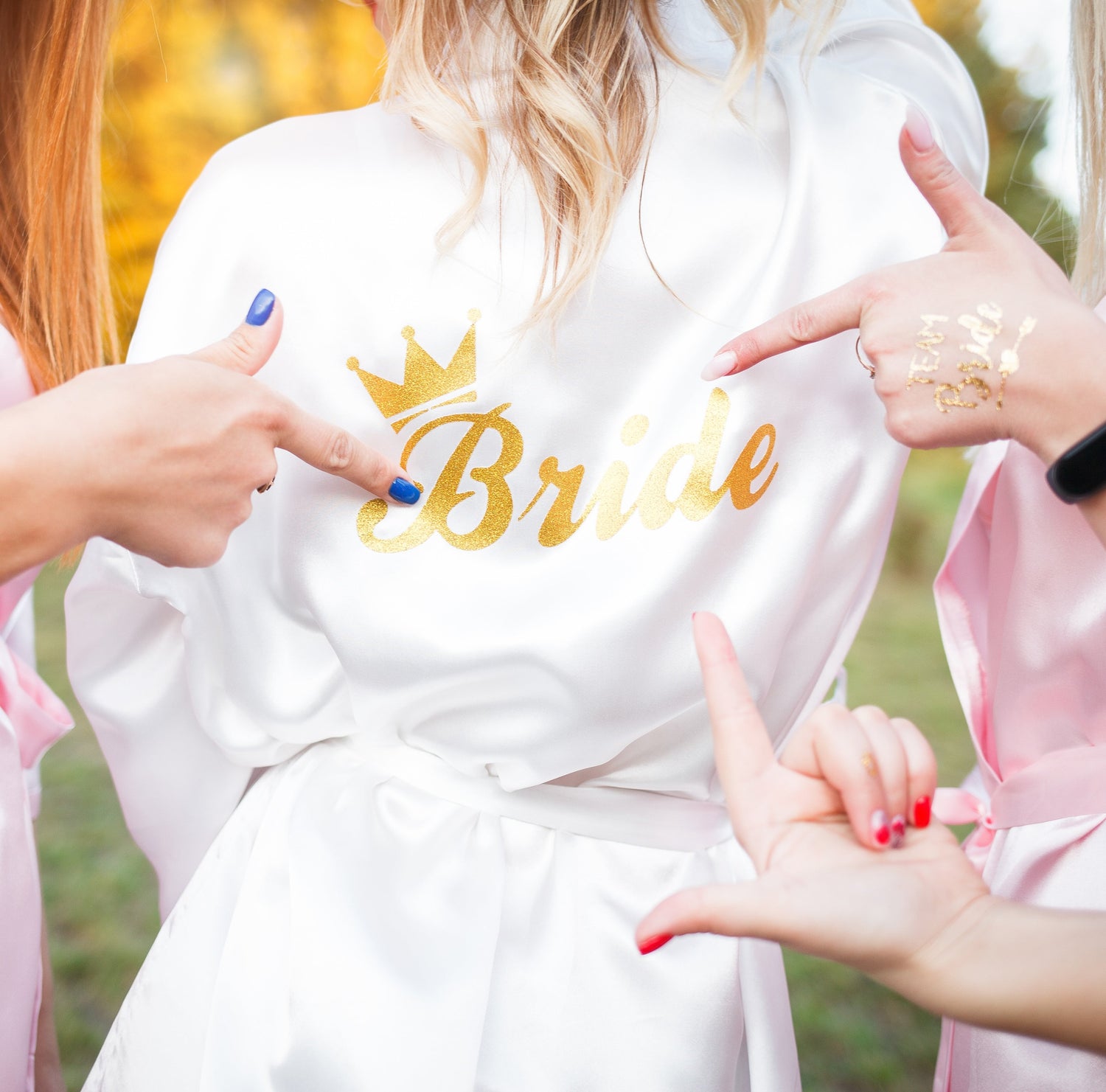 Back of bridal robe with ‘Bride’ on it, surrounded by hands pointing at the text – perfect bride squad moment