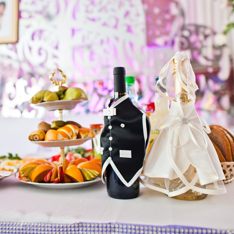 Wedding reception table, decorated with a food serving tower and two small bottles of champagne decorated in a mini bride's dress and groom's suit.