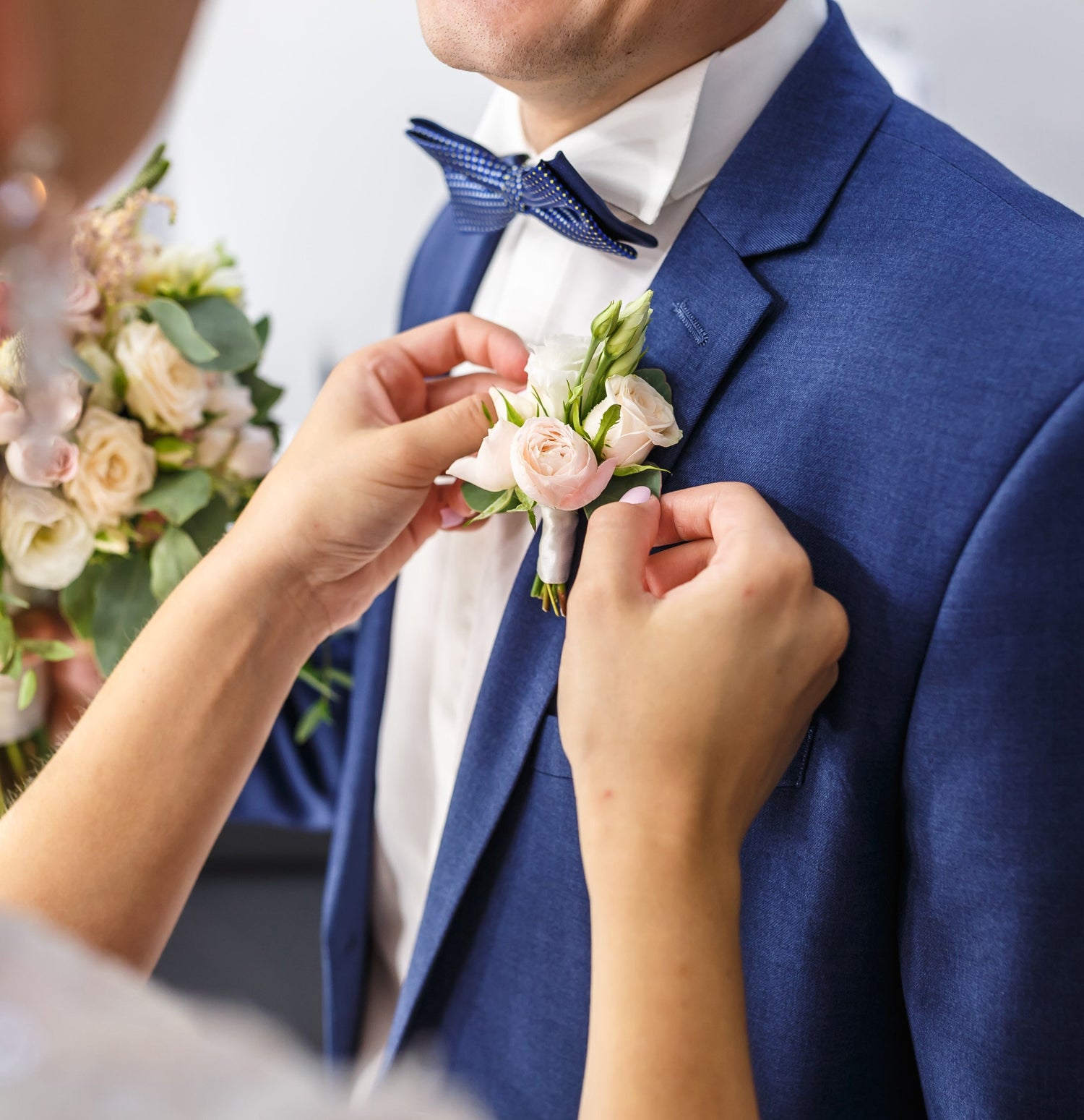 A woman places a floral wedding buttonhole on a man's suit.