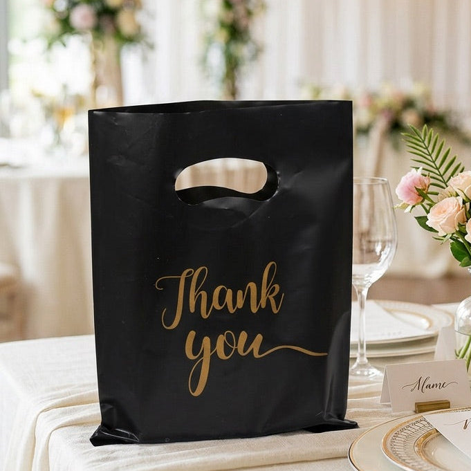 Black 'Thank you' bag on a table with floral arrangements and glasses.