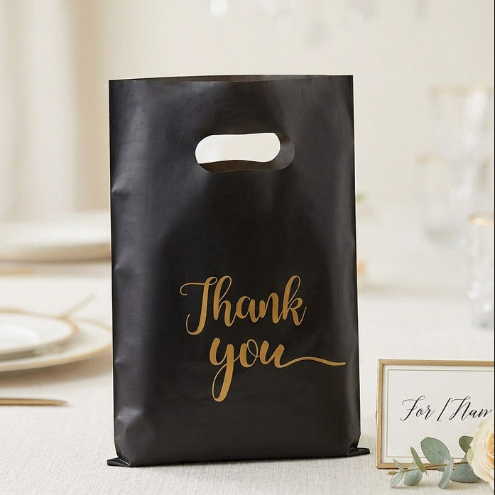 Black 'Thank you' bag on a table with floral decorations and glasses.