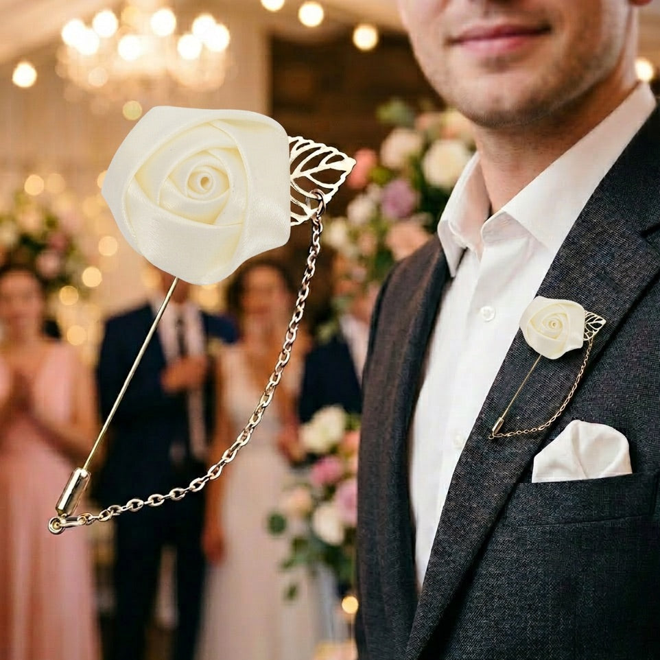 Man in a suit with a white rose lapel pin and matching pocket square in a blurred indoor setting.