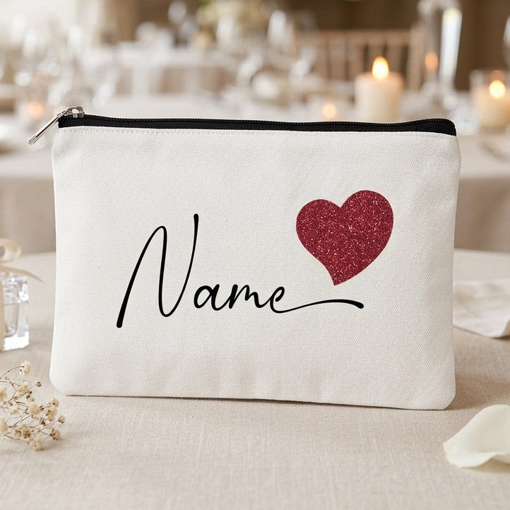 White make up bag with red heart and 'Name' text on a table setting with candles and decor.