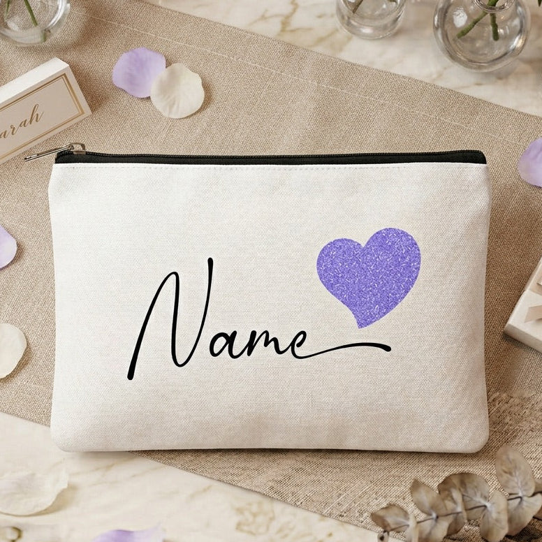White make up bag with purple heart and 'Name' text on a decorative surface with candles and flowers.