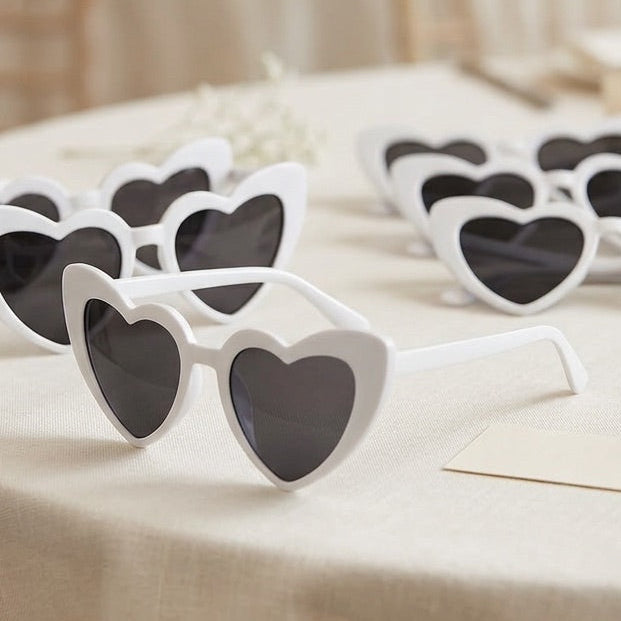 Heart-shaped sunglasses on a table with a blurred background of lights and flowers