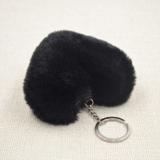 Black fluffy keychain with a metal keyring on a beige background