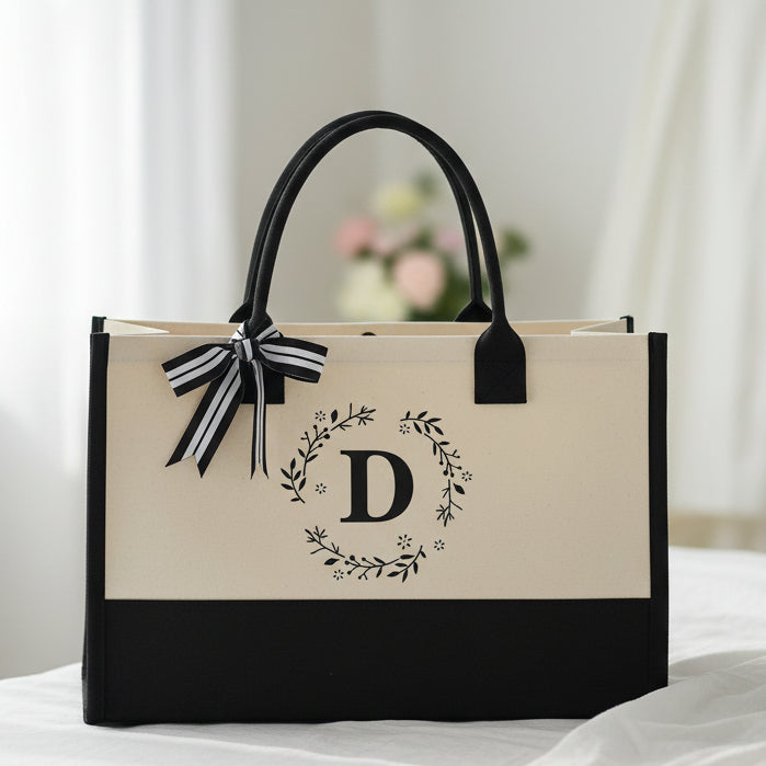 White tote bag with black accents, floral arrangement, and book on a white background