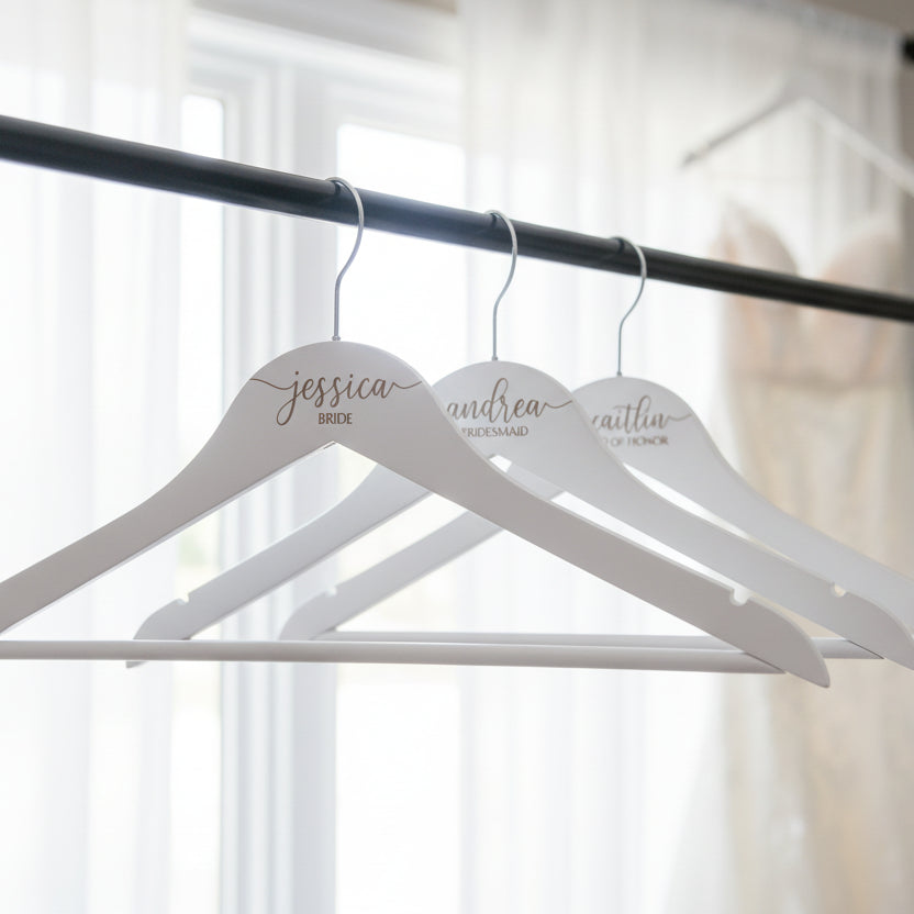 Three white hangers with personalized names on a black rod against a gray background