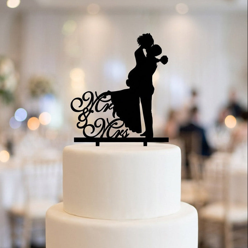 White wedding cake with a black silhouette topper in a blurred indoor setting