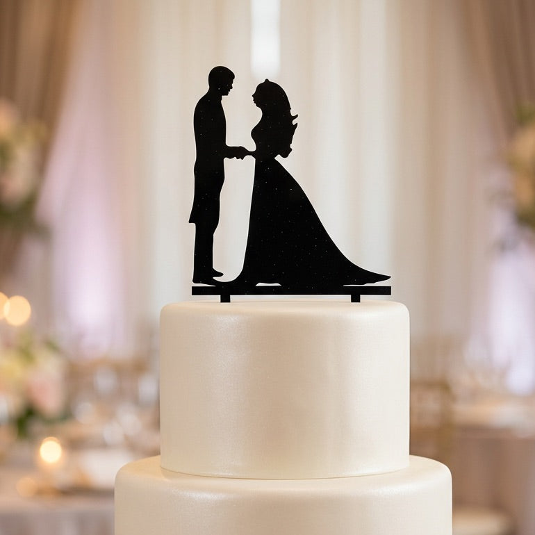 White wedding cake with a black silhouette topper of a couple in an elegant setting.