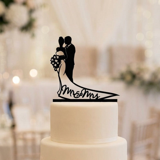 White wedding cake with a black 'Mr. & Mrs.' topper in a festive setting.